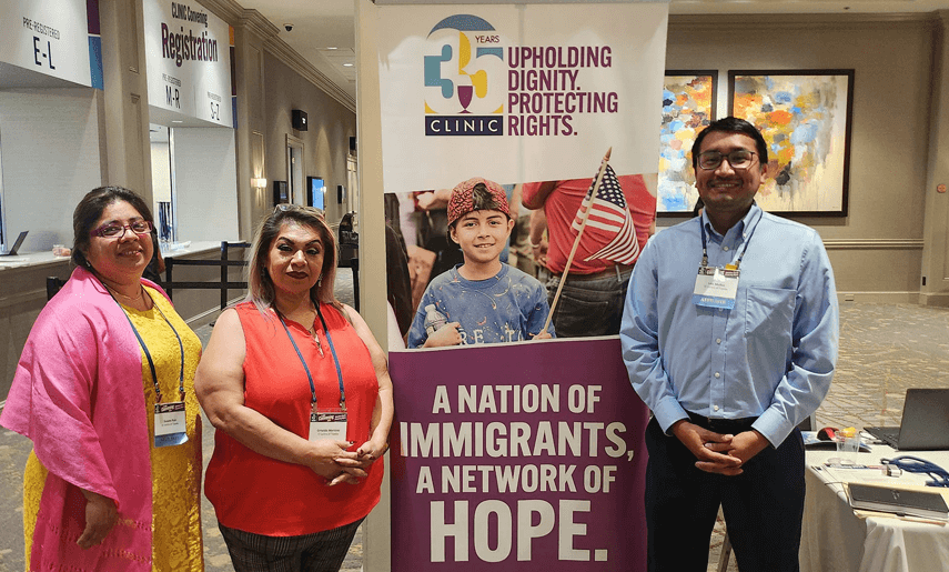 Gris and Lalo standing with a community leader by a pull-up banner at a local community event.